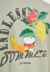Camiseta de algodón verde claro con un gráfico floral que presenta flores rojas y limones amarillos, acompañada de "VERANO INFINITO" en letras negras en negrita.