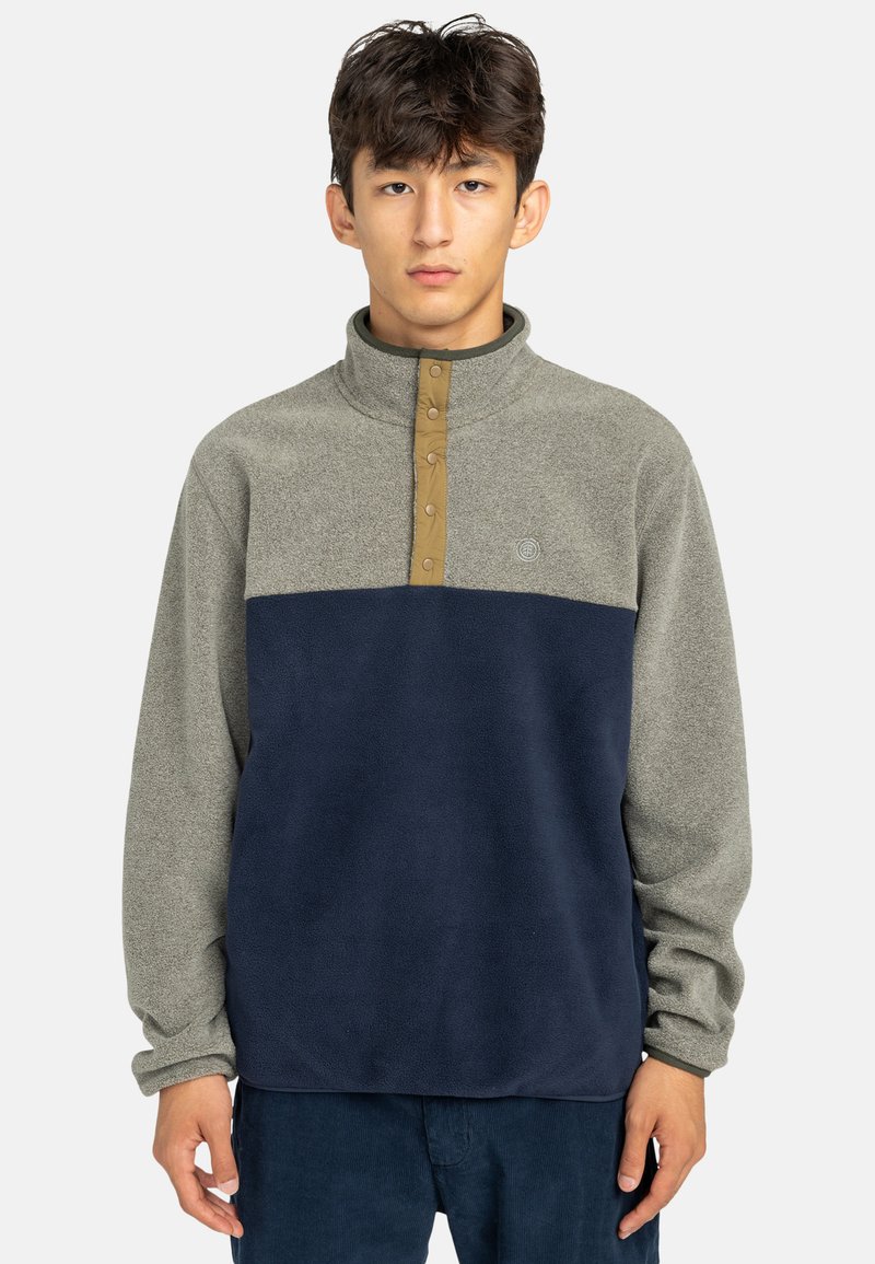 Fleece pullover met een groen-grijze bovenkant, navy onderkant, knoopsluiting bij de hals en logo detail op de borst. Zachte textuur en een relaxte pasvorm.