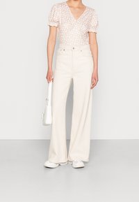 Jeans anchos de talle alto en blanco combinados con una blusa de estampado floral en rosa claro, con mangas abullonadas y escote en V. También incluye zapatillas blancas y bolso.