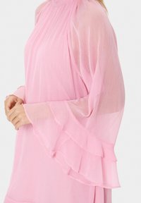 Rosa durchsichtige Bluse mit Rüschensäumen und plissiertem Design. Leichter Stoff bietet eine weiche Textur. Taillierter Schnitt betont die Silhouette.