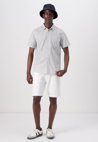 Kortærmet stribet skjorte i grå og hvid, parret med hvide shorts. Tilbehør inkluderer en sort spandhat og grå og hvide sneakers.