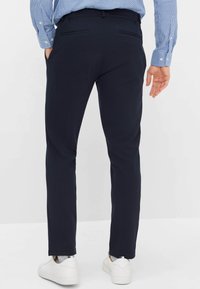 Marineblauwe chino's met een smalle pasvorm, voorzien van zakken en een gladde stoftextuur. Gecombineerd met witte sneakers en een blauw geruit overhemd.