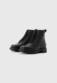 Botas de tobillo de cuero negro con acabado texturizado, punta redondeada, cierre de cordones en la parte delantera y suela de goma resistente. Incluyen una lengüeta en la parte trasera.