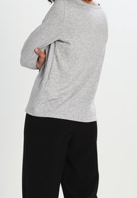 Graues Langarmoberteil aus weichem Stoff, mit Rundhalsausschnitt und lockerer Passform, kombiniert mit schwarzen Hosen. Die Textur wirkt glatt.