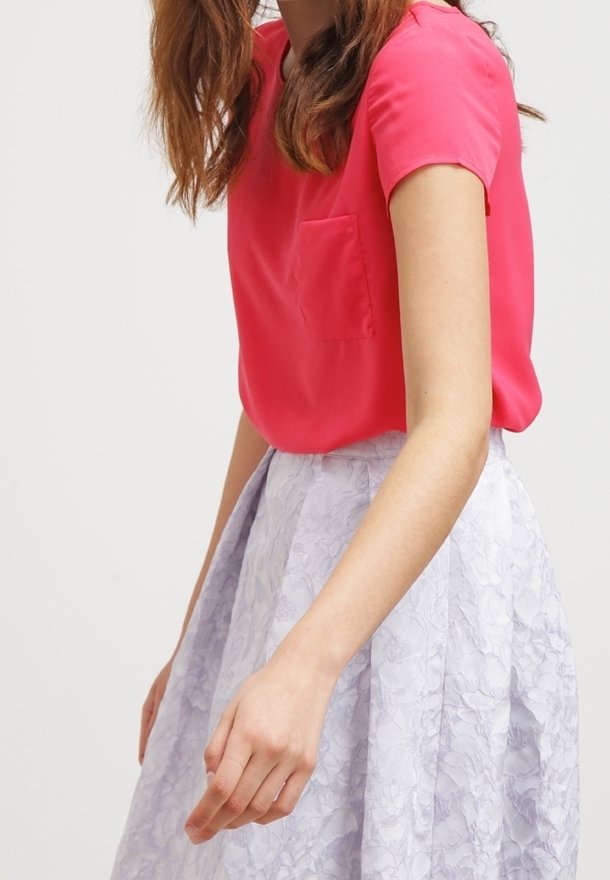 Růžový top s krátkými rukávy a kapsou na prsou, doplněný texturovanou světle fialovou sukní s květinovým vzorem.