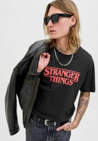 Černé bavlněné tričko s červeným logem "STRANGER THINGS", v kombinaci s černou koženou bundou a stříbrným řetízkem. Tmavé džíny.