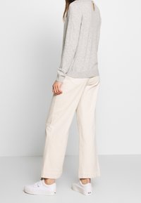 Pull en tricot gris avec un détail en fente au dos, assorti à un pantalon large crème et des baskets blanches. Mettez l'accent sur les textures douces et la coupe décontractée.