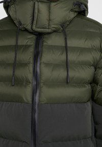 Grøn og mørkegrå polstret jakke med sort lynlås foran og hætte snore, der viser detaljerede bryst- og overarmssektioner.