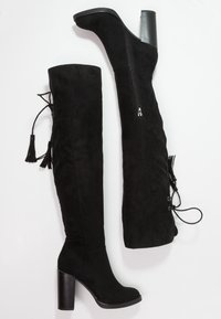 Stivali alti in suede nero presentano una punta tonda, un tacco a blocco alto, una cerniera laterale e frange decorative con lacci sul retro.