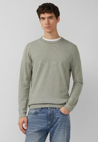 Lichtgroene trui met lange mouwen en een geribde ronde hals. Heeft een gestructureerd patroon en aansluitende boorden, gecombineerd met lichtblauwe spijkerbroek.