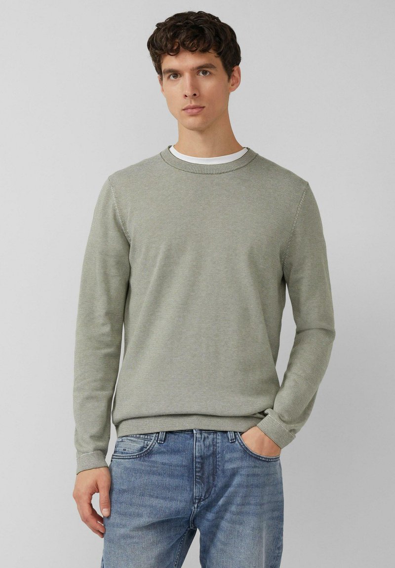 Lichtgroene trui met lange mouwen en een geribde ronde hals. Heeft een gestructureerd patroon en aansluitende boorden, gecombineerd met lichtblauwe spijkerbroek.