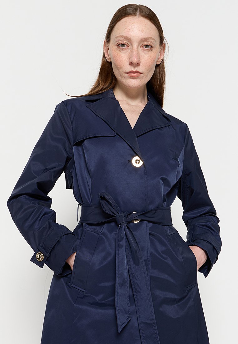 Soprabito blu navy con vita legata, ampio colletto e dettagli con bottoni dorati; realizzato in tessuto morbido e lucente, con tasche laterali.