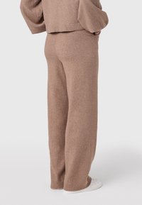 Beige pletené kalhoty na domácí nošení, rovný střih, měkká textura, elastický pas, v kombinaci s bílými teniskami.