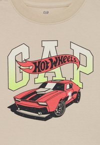 Beige t-shirt med et grafisk motiv af en rød bil med sorte striber og teksten "GAP Hot Wheels" i sort og neongul.