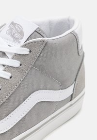 Szare płócienne sneakersy z białymi skórzanymi akcentami, z białymi sznurowadłami i metką z logo na języku. Zauważalna fakturowana powierzchnia i przyszyte detale.