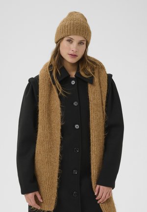Schwarzer Mantel mit Knopfverschluss, strukturierter beige Schal und passender gerippter Strickmütze. Der Mantel hat einen Kragen und gepolsterte Schultern.