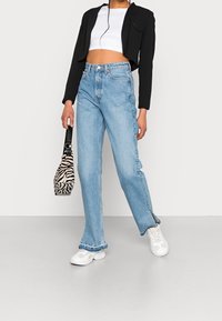 Jean taille haute bleu clair avec une jambe droite, ourlet effiloché, associé à une veste noire courte et un sac à main à motifs zèbres.