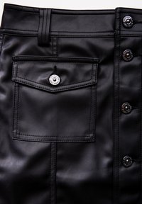 Černá sukně z umělé kůže s přední kapsou, zapínáním na knoflík s metalickými akcenty a viditelnými švy. Hladká textura.