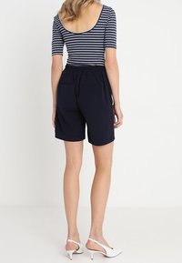 Námořnické modré kraťasy s elastickým pasem, dvěma zadními kapsami a hladkým povrchem, spárované s pruhovaným topem s kulatým výstřihem.