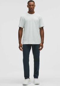 Camiseta de manga corta gris claro combinada con pantalones oscuros de corte slim-fit y zapatillas blancas. Diseño casual y contemporáneo con un ajuste relajado.