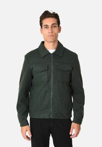 Giacca in misto lana verde con chiusura a zip, due tasche sul petto e colletto classico, realizzata in tessuto texturizzato e con silhouette aderente.