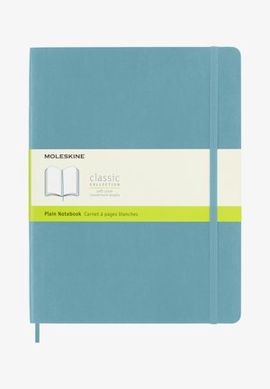 Taccuino Moleskine con copertina morbida, caratterizzato da una copertura color teals, chiusura con elastico e un'etichetta gialla con i dettagli del prodotto.