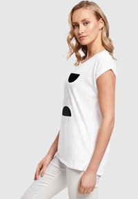 Hvid bomulds-t-shirt med opkrøllede korte ærmer, der har sorte geometriske mønstre og linjer foran. Stylet med lysegrå slim-fit bukser.