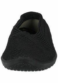 Chaussure noire à enfiler en matériau tricoté texturé, avec un bout arrondi, une semelle flexible et un motif en vagues discret sur le dessus. Pas de branding visible.