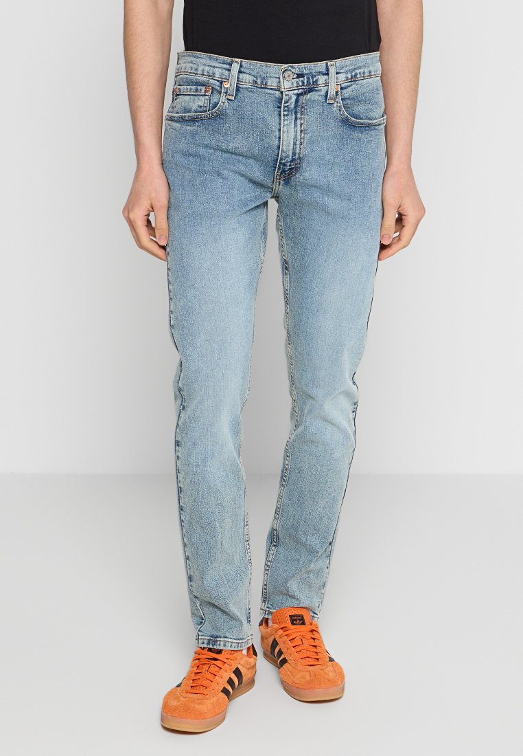 Jeans de mezclilla azul claro con un corte recto, diseño de cinco bolsillos y un desgaste sutil; combinados con zapatillas de ante naranjas.