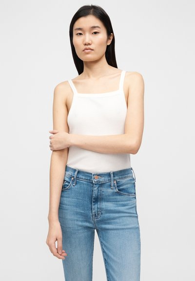 Fehér bordázott ujjatlan felső négyzet alakú nyakkivágással és vékony pántokkal, világoskék, magas derekú farmerrel párosítva. Sima textúra, letisztult dizájn.