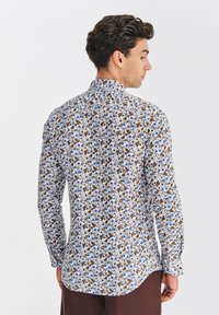 Koszula z długim rękawem w kolorze białym z kwiatowym wzorem w odcieniach niebieskiego, brązowego i zielonego. Posiada klasyczny kołnierzyk i zapinane na guziki mankiety.