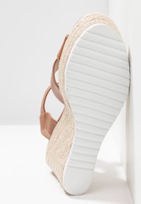 Sandale compensée en cuir marron avec une semelle intermédiaire tissée de style espadrille et une semelle extérieure en caoutchouc blanc, présentant un design de talon courbé et de sangles.