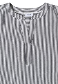 Chemise à rayures verticales noires et blanches avec col rond et encolure à fente frontale portant une étiquette de la marque CECIL.
