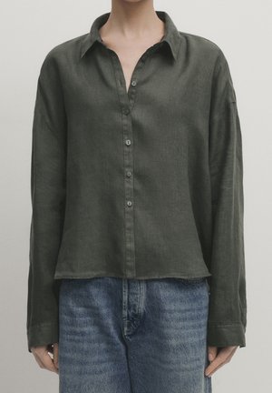 Donkergroen, overhemd met lange mouwen, knopen en een kraag, met een losse pasvorm. Zachte textuur en licht gecropt zoom, gecombineerd met een blauwe spijkerbroek.
