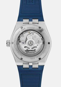Zegarek ze stalową kopertą i przezroczystym deklem, z automatycznym mechanizmem, niebieskim paskiem silikonowym i wyraźnym logo Ingersoll.