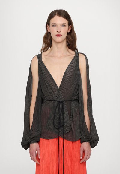 Blouse noire à plis avec décolleté en V profond, manches longues et ceinture noire à la taille, associée à une jupe plissée orange vif.