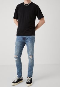 Camiseta negra de manga corta con un bolsillo en el pecho, combinada con vaqueros desgastados de color azul claro y zapatillas negras con suelas blancas.
