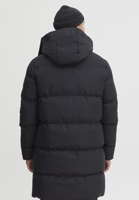 Sort pufferjakke med hætte, der har et quiltet design og en glat overflade. Jakken har en lang silhuet og elastiske manchetter.