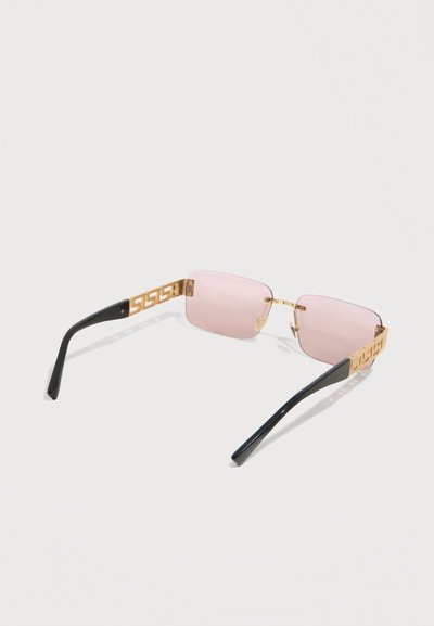 Ορθογώνια γυαλιά ηλίου με ροζ απόχρωση και γεωμετρικές χρυσές λεπτομέρειες στα μαύρα πλαϊνά, εμφανιζόμενα από σκιασμένη πίσω γωνία σε λευκό φόντο.