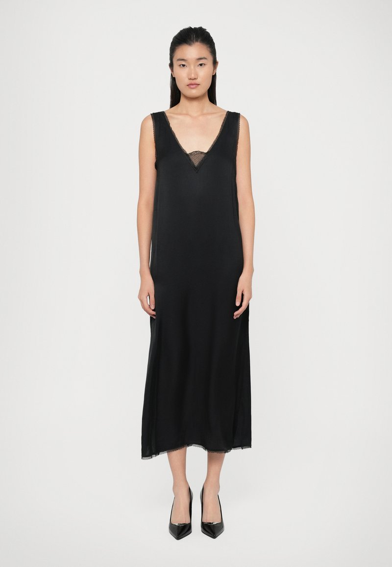 Black satin slip dress with a V-neckline and lace trim, flowing silhouette, and above-ankle length. Complemented by pointed black heels.