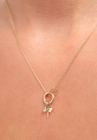 Gouden halsketting met twee in elkaar grijpende ringen, met kleine decoratieve hangers: een hart, een kristal druppel en een kleine hanger, aan een fijne ketting.