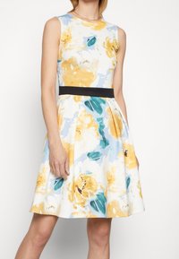 Vestido floral con un patrón de flores azules y amarillas, diseño sin mangas, corsé ajustado, cinturilla negra y falda acampanada. Material de algodón.