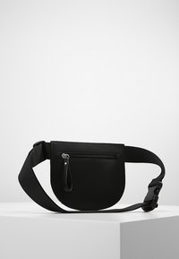 Musta, pyöreä vyölaukku, joka on valmistettu sileästä materiaalista. Siinä on vetoketjutasku edessä ja säädettävä hihna käytettäväksi. Yksinkertainen muotoilu.