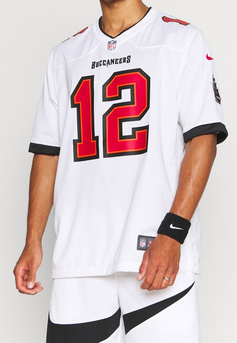 Homme portant un maillot blanc des Tampa Bay Buccaneers NFL avec le numéro 12, un short blanc avec une bande noire et un bracelet Nike noir.