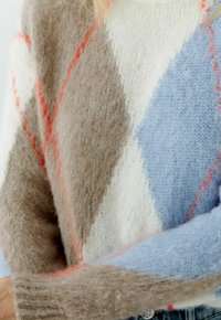 Gebreide trui in beige, crème en lichtblauw. Voorzien van een ruitpatroon met perzikkleurige accenten en geribbelde manchetten. Zachte, pluizige textuur.