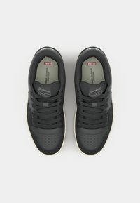 Black composite sneakers feature a smooth texture, perforated toe cap, and gray accents. The soles are cream-colored with textured tread.