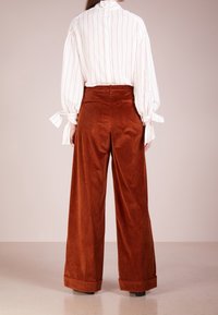 Biała i czerwona bluzka w paski z bufiastymi rękawami, zestawiona z szerokimi, brązowymi spodniami z kordurowej tkaniny z mankietem i tylnymi kieszeniami.