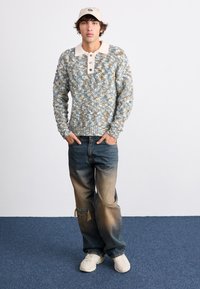 Textured blue and cream knit sweater with a collared neckline and three buttons, paired with faded blue jeans and white sneakers.