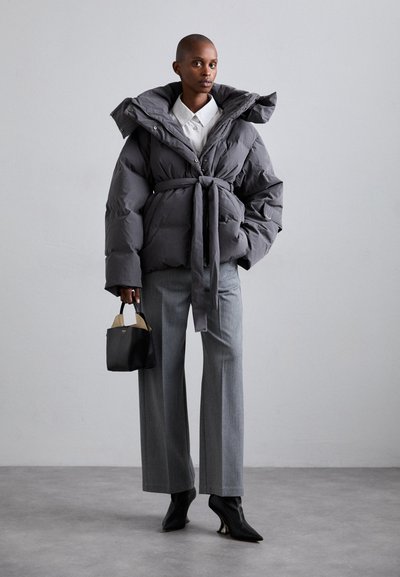 Grey puffer jacket with a belted waist, high collar, and side pockets. Paired with grey wide-leg trousers and black heeled ankle boots.