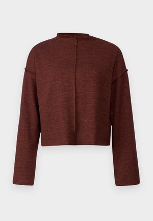 Lühendatud pullover tumesinises, valmistatud tekstuurilisest kangast. Omab pikki varrukasid ja kõrget kaelust, mille tagaküljel on nupu detail.